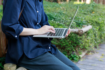 公園でノートパソコンを使用している女性　屋外　仕事　イメージ