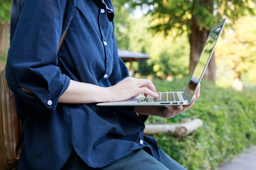 公園でノートパソコンを使用している女性　屋外　仕事　イメージ