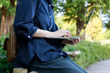 公園でノートパソコンを使用している女性　屋外　仕事　イメージ