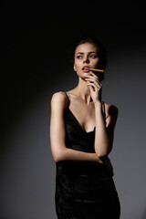 Elegant woman in black dress poses thoughtfully against a dark background, exuding confidence and...