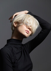 Stylish young woman with short blonde hair posing against a gray backdrop, showcasing modern fashion and confidence. Portrait and beauty concept.