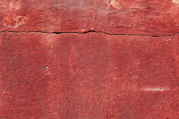 Red texture of a concrete wall with natural relief and damage in the form of chips and scratches. Fragment of an old stone surface with a crack. Dark rough surface with a place for an inscription