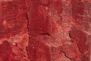 Red texture of a concrete wall with natural relief and damage in the form of chips and scratches. Fragment of an old stone surface with a crack. Dark rough surface with a place for an inscription