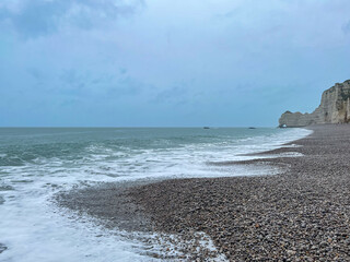 Beautiful seascape of sea waves on a pebble rock beach on a cloudy day in Normandy, France