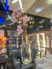 Fototapeta premium Vintage glass bottle with bouquet of cherry blossoms in a glass vase in a cafe hanging in the air