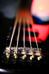 Electric bass guitar 5 strings illuminated with red light, blur background.