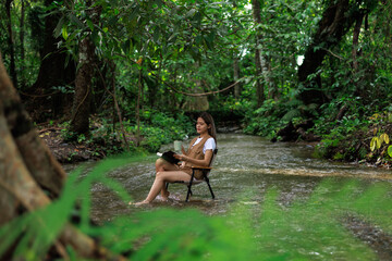 woman sitting on a chair in the stream and drinking coffee with a book in her hand