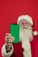Naklejka premium Santa claus holding smartphone with green chroma key screen on red background