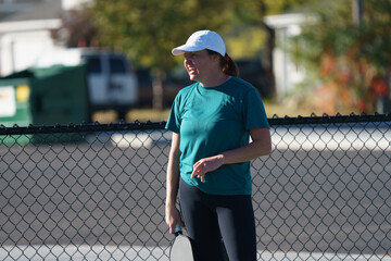 woman wearing white hat playing pickle ball on outdoor pickleball court