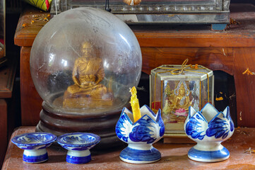 A dusty home altar with figures of Buddha and a monk