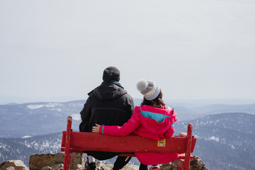 a loving couple sitting on a bench on top of a mountain