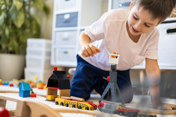 A small white-skinned European child builds a toy railway at home on the carpet. The boy plays
