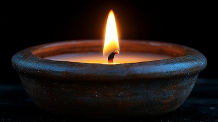 A single candle flame in a brown ceramic holder, burning brightly against a black background.