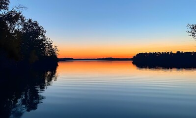 Obraz premium lake reflecting the colors of an evening sky, with silhouettes of trees in the background