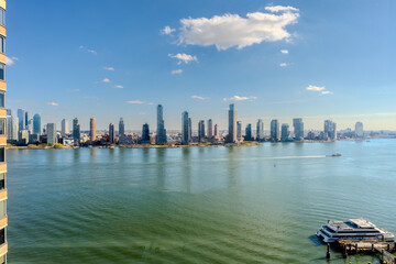 Naklejka premium A beautiful autumn day on the Hudson River, with warm sunlight illuminating the water and enhancing the vibrant energy of NYC against the serene river backdrop. The scene captures a ferry gliding
