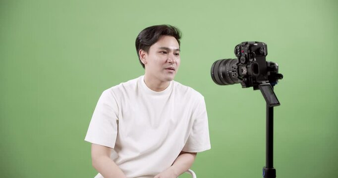 Handsome young content creator with a bright smile, preparing and explaining his video recording process for sharing online, set against a vibrant green background.