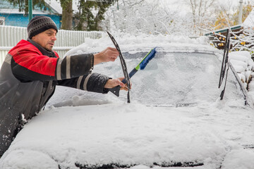 A European man clears snow from the windshield of a car.