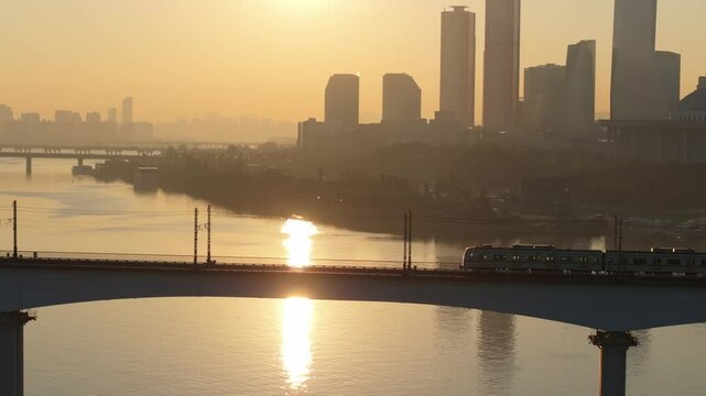 A subway train crossing Dangsan Bridge in Seoul against a backdrop of a reddish-yellow sunrise
