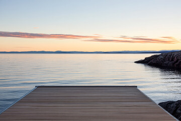 Fototapeta premium Tranquil wooden dock extending into calm waters at sunset in a coastal landscape