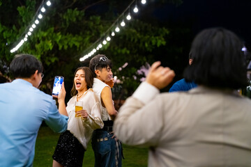 Group of Happy Asian millennial generation people friends enjoy and fun celebration reunion meeting outdoor dinner party with drinking beer and dancing in the garden at restaurant on holiday vacation.