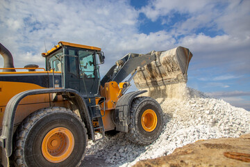 a yellow bucket truck dumps white marble chips onto an open warehouse at the wharf. A bucket loader forms a stack