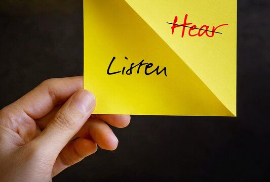 Hand holding paper note with handwritten text HEAR replaced with LISTEN - concept of practice active listening , focus and try to understand what speaker really want to communicate