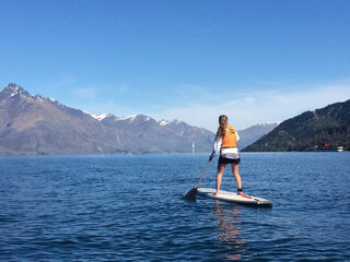 woman standup paddleboarding on lake wakatipu, new zealand
