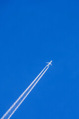 Commercial airplane with white vapor trail flying on a blue sky