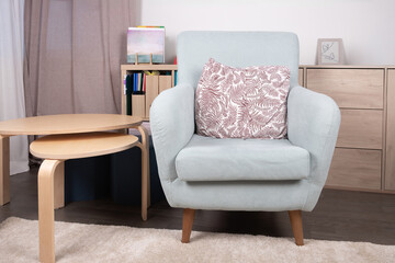 Light colored one-seater armchair with cushion in a bright living room with wooden furniture. Minimalist interior concept and decoration