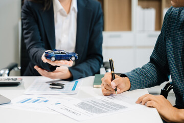 Business professionals finalize a car sale agreement with paperwork and model car, capturing themes