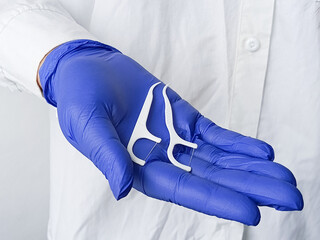 Dentist in white coat and blue medical gloves holds plastic flosser in hand. Recommendations for cleaning teeth. Oral hygiene.