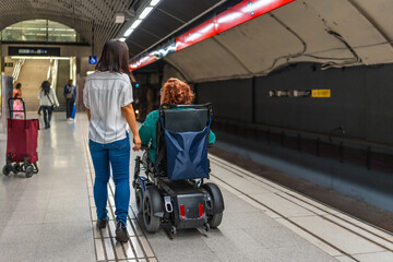 Woman in wheelchair and friend walking along metro station