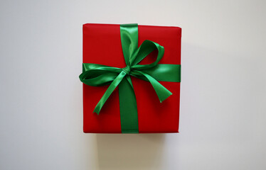 Gift isolated on white background. Square box. Red wrapping paper. Green ribbon and bow. Placed in the center of the background. Christmas, birthday, New Year, greetings. Traditional colors.