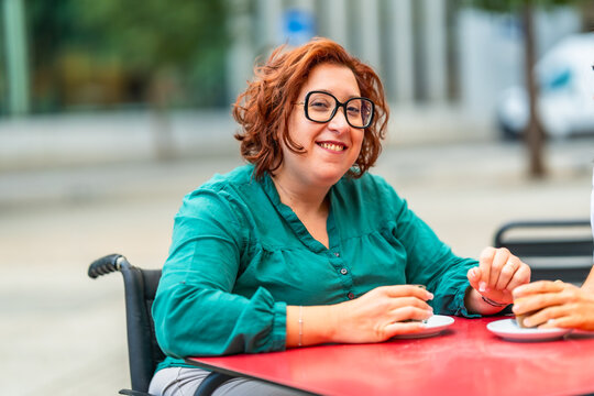 Woman with disability using electric wheelchair drinking coffee with friend