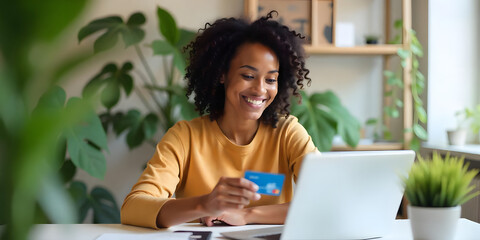 Beautiful woman in her 30s, sitting at her desk and holding a credit card with her hand while making an online purchase on her laptop
