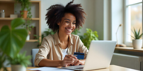 Beautiful woman in her 30s, sitting at her desk and holding a credit card with her hand while making an online purchase on her laptop