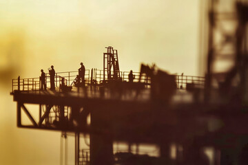 Silhouettes of oil and gas workers performing tasks on an industrial platform near an oil well during daylight hours