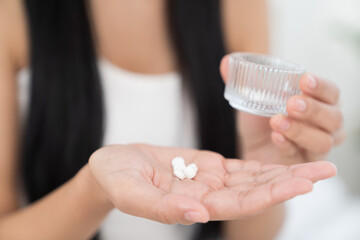 Young Asian woman taking pill while sitting on bed in the bedroom at home. Asian woman stressed and sick