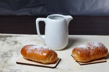 Homemade buns with jam with powdered sugar on wooden background. Fresh bakery and milk jug on kitchen table. Sweet breakfast