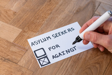 human hand with marker casts negative vote on popular trending topic asylum seekers. public opinion...