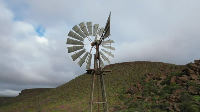 Old metal windpump turning slowly in remote South African landscape under cloudy skies