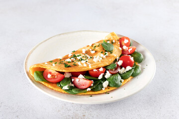 Stuffed omelette with tomatoes, cheese and spinach on a white background. 