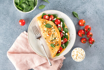 Stuffed omelette with tomatoes, cheese and spinach on a blue background. Top view. 