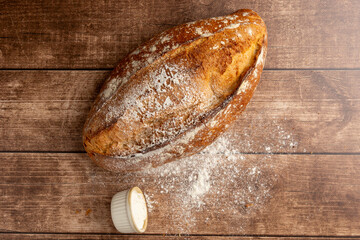 A freshly baked, rustic artisan bread loaf on a wooden table, accompanied by a dusting of flour and a metal sieve, evoking a sense of home baking and coziness.