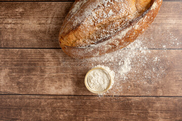 A freshly baked, rustic artisan bread loaf on a wooden table, accompanied by a dusting of flour and a metal sieve, evoking a sense of home baking and coziness.