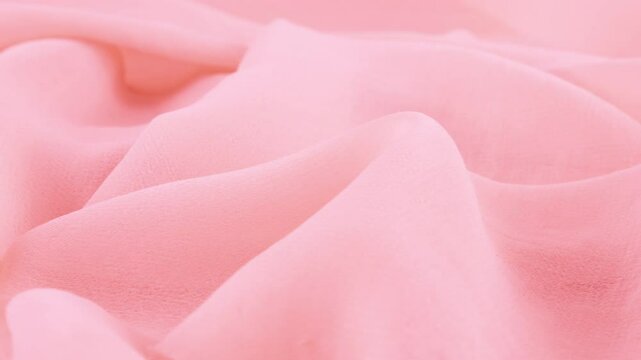 Close-up view of the soft folds of thin light taffy pink color chiffon fabric on a rotating display case. Textile background with sewing accessories on the theme of fashion, design, fabrics.