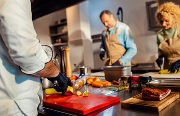 Middle-aged couple enjoying a cooking class with a chef preparing zucchini for a meal in the kitchen.
