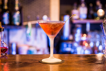 Frozen martini glass standing on a wooden table and colorful lights in the background