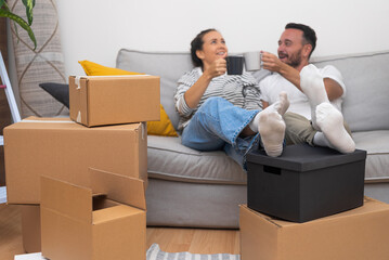 Pretty woman with lovely husband relaxes celebrating moving sitting on contemporary sofa sorting out boxes of things for fancy interior in new house in countryside