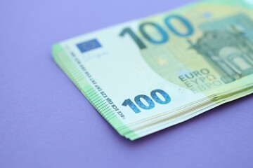 Big amount of one hundred euro money bills on lilac background